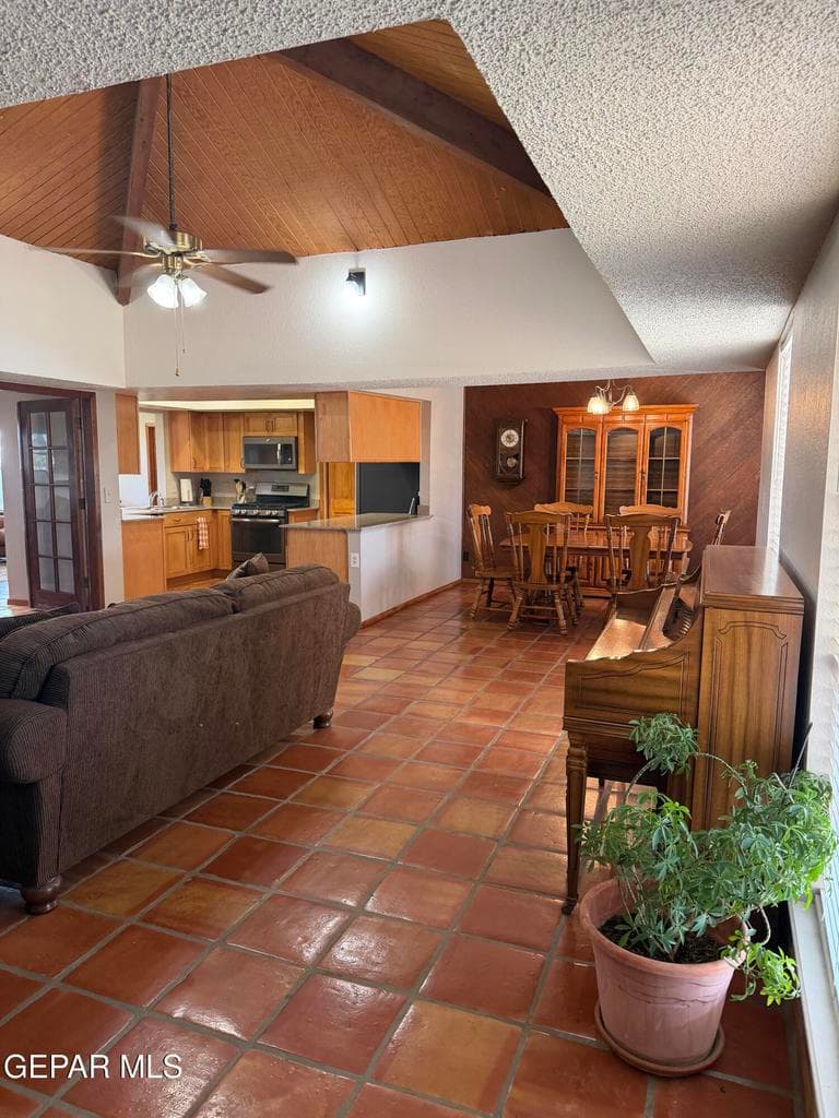 Vaulted ceiling with exposed wood paneling, terra-cotta tile flooring, kitchen featuring light wood cabinetry, and a French door entry
