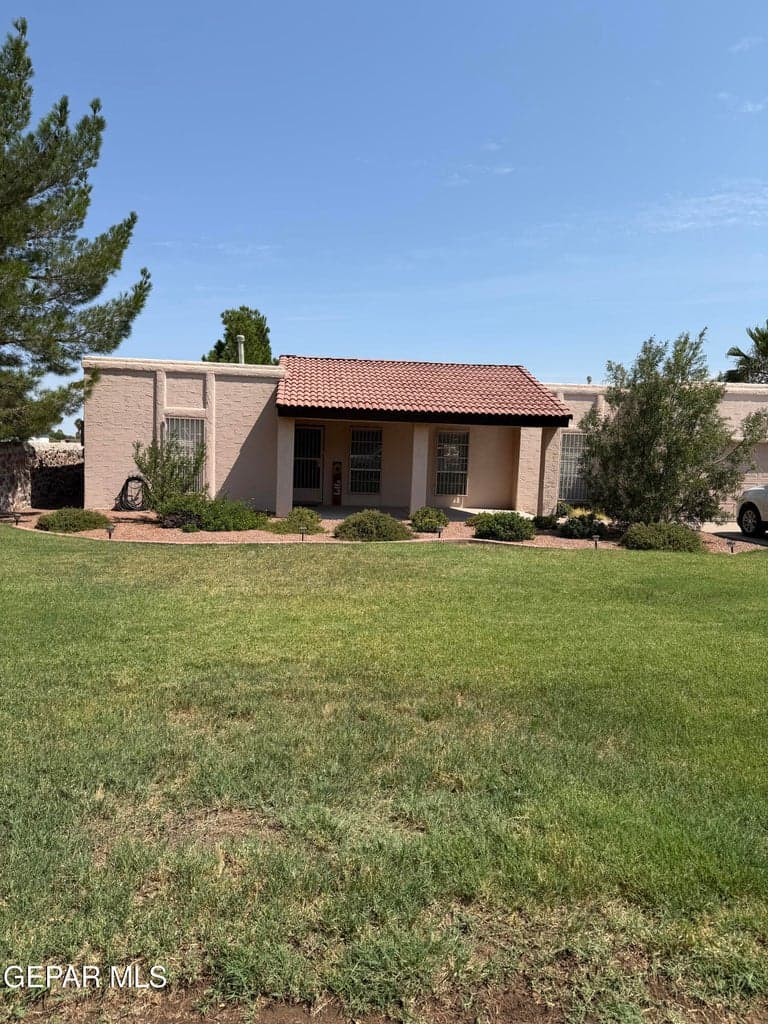 Single-story exterior featuring a stucco facade, red tile roof, covered entryway, and expansive grass lawn