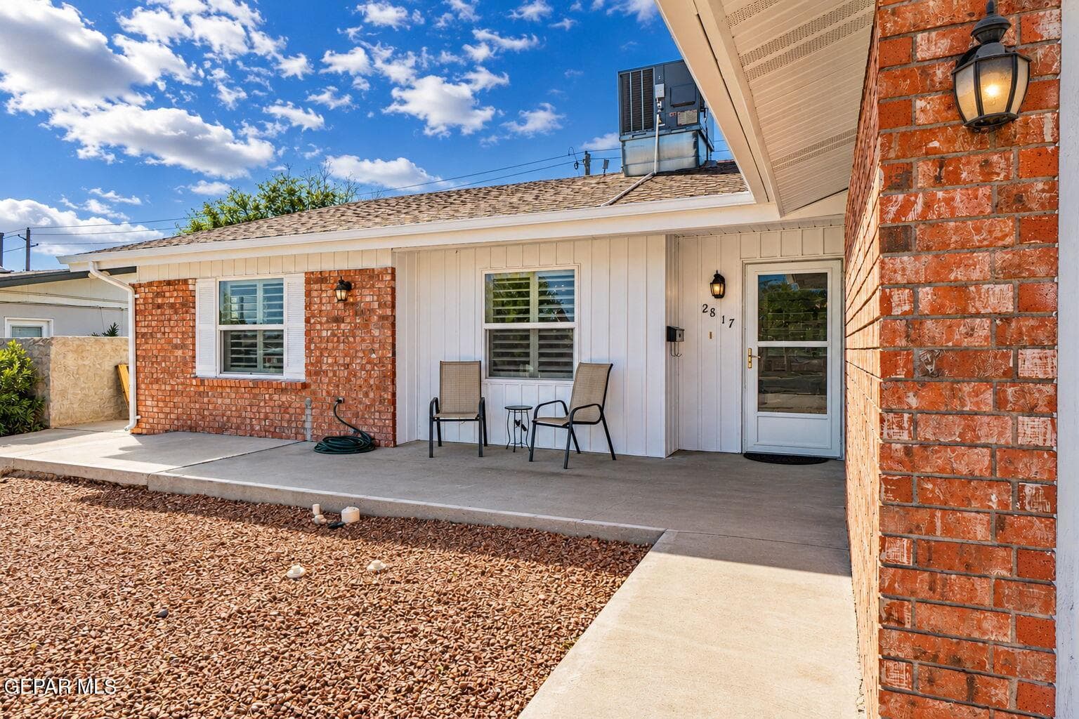 Exterior featuring a combination of red brick and vertical siding, a covered concrete patio, and an entry door with glass paneling