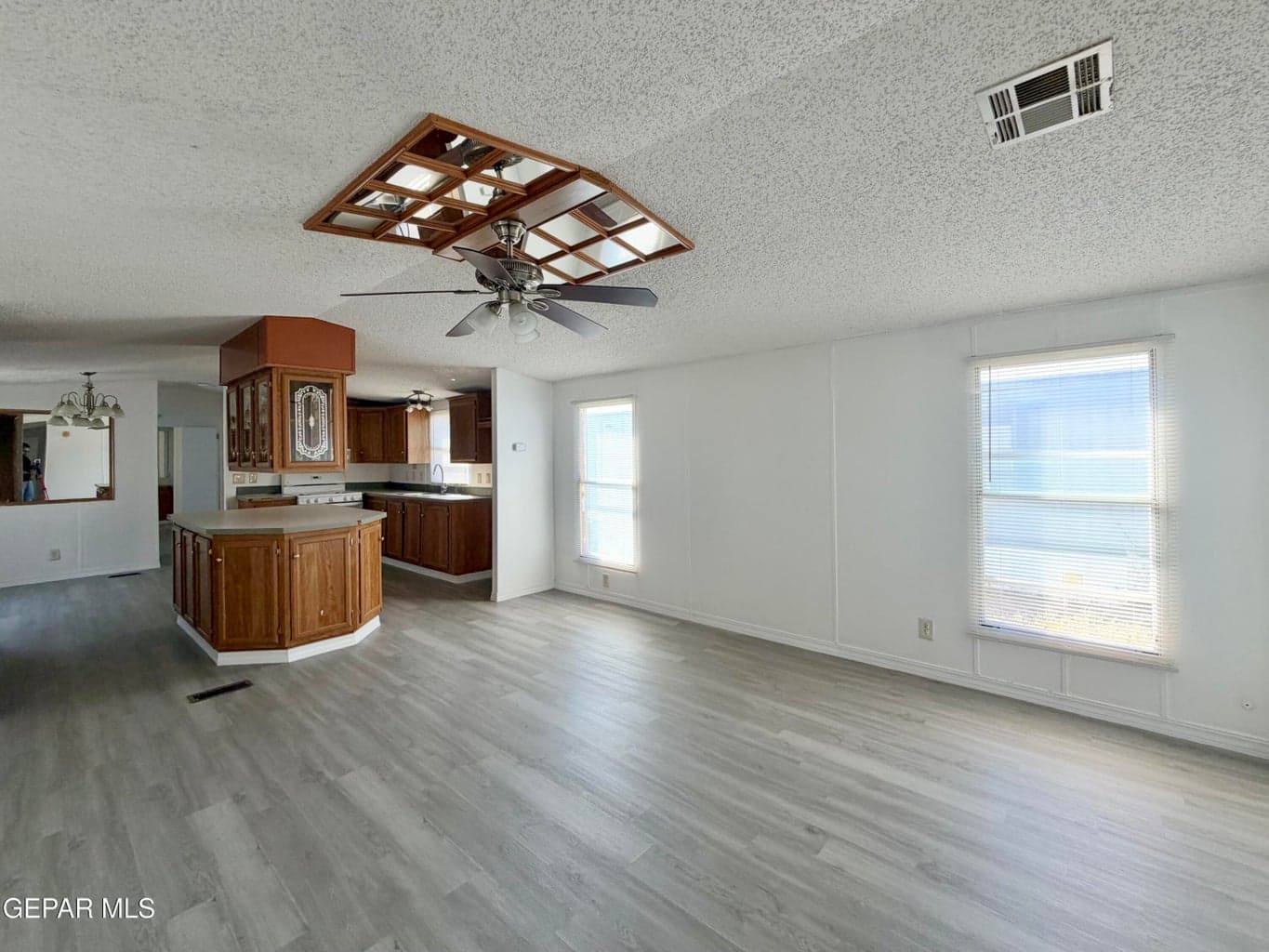 Open-concept interior featuring wood-finish flooring, a kitchen island with built-in cabinetry, recessed ceiling panel lighting, and multiple windows