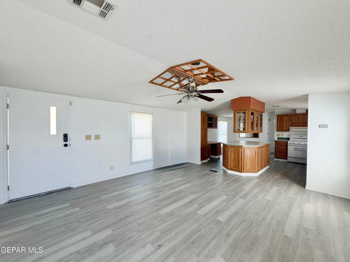 Wood-finish flooring, ceiling fan with decorative geometric trim, and a kitchen featuring wood cabinetry with a wrap-around breakfast bar