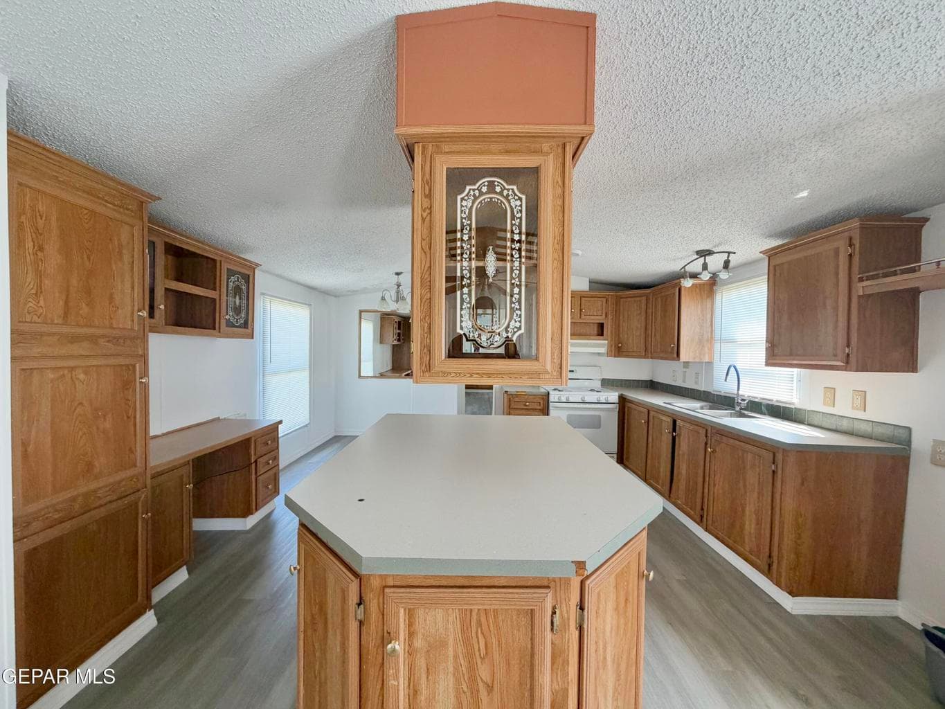 Kitchen featuring wood cabinetry, central island with composite countertop, built-in desk area, and wood-finish flooring