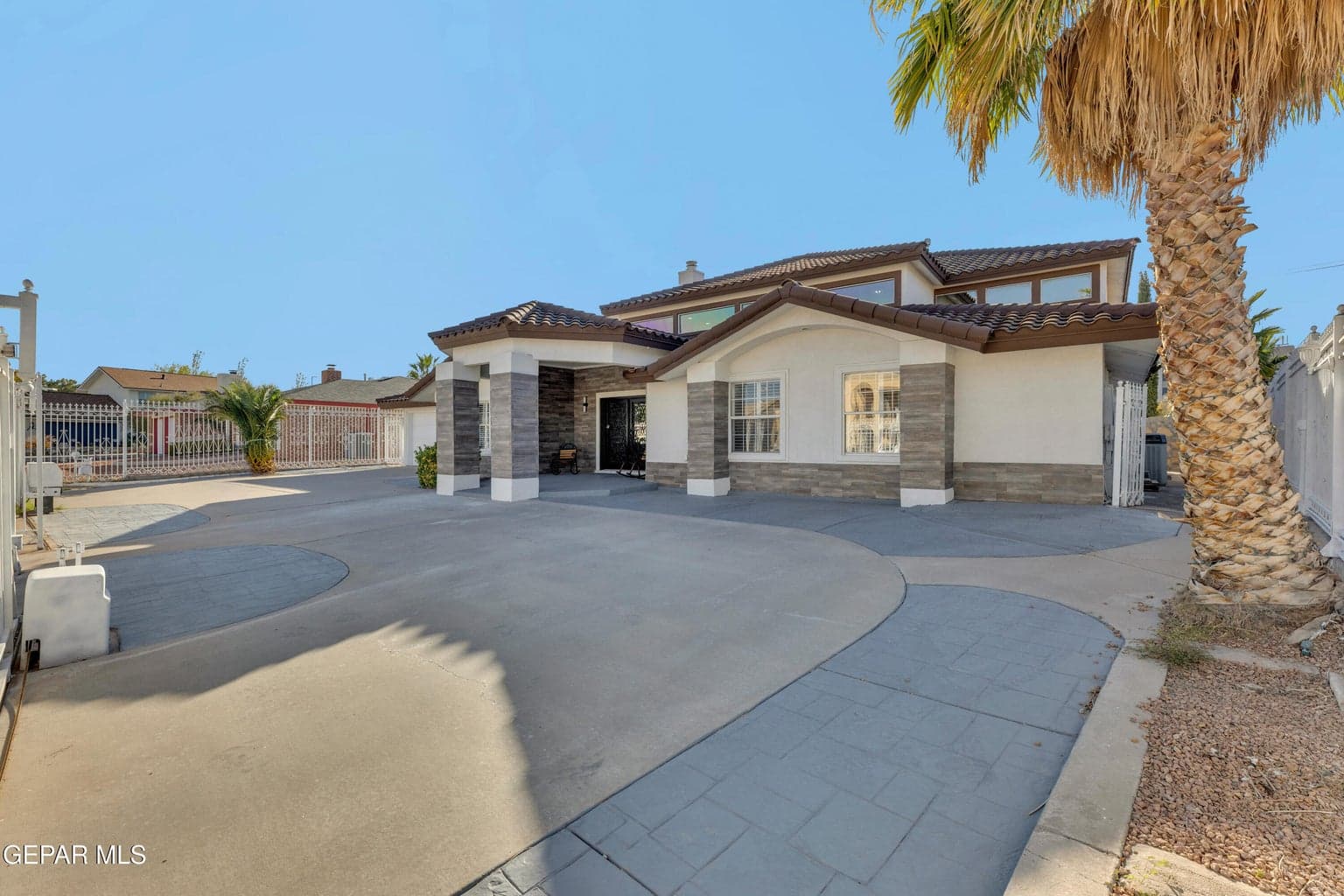 Stucco exterior with stone veneer accents, multi-gabled tile roof, and expansive concrete driveway with patterned paving details