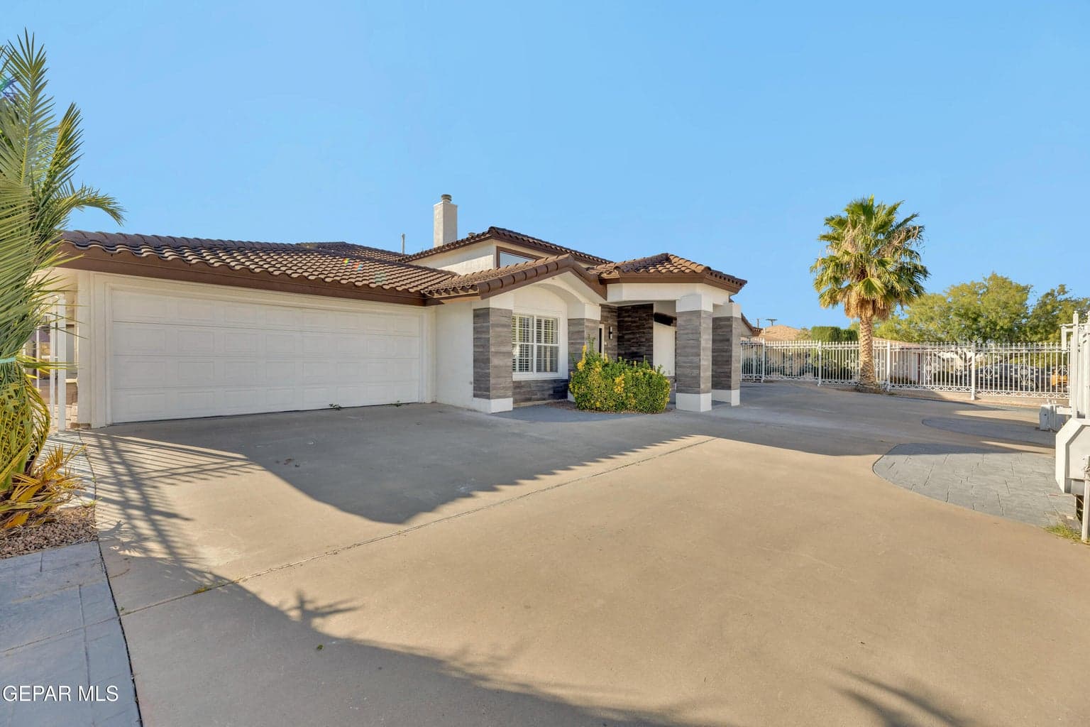 Single-story residence featuring a tile roof, neutral stucco exterior, stone masonry accents, a multi-car garage, and gated hardscaped entry