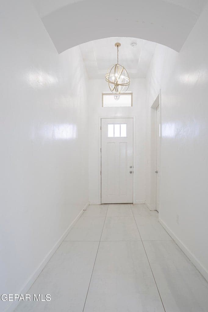 Entryway featuring an arched ceiling, large-format tile flooring, chandelier, and a front door with glass transom window