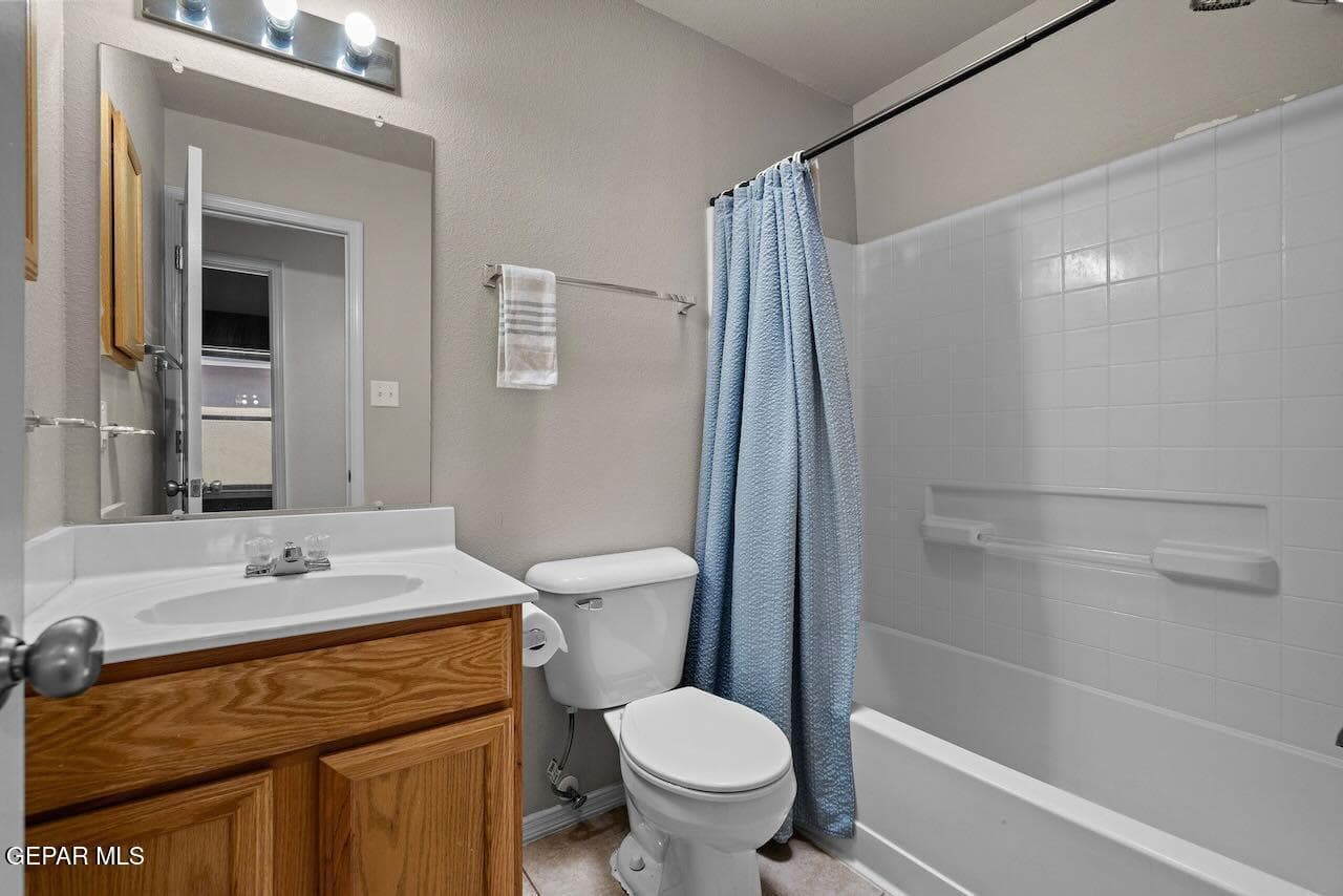 Bathroom featuring a wood-finish vanity with a white countertop and oval basin, a recessed tub and shower combination with white tile surround, and a large wall-mounted mirror